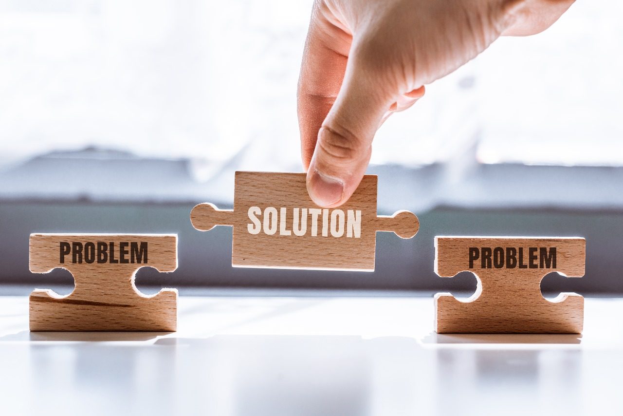 A hand placing a wooden jigsaw piece labelled Solution between two pieces labelled Problem