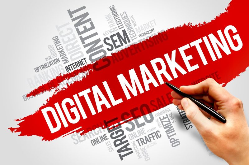 The words Digital Marketing over a word cloud of marketing terms, with a hand holding a pen