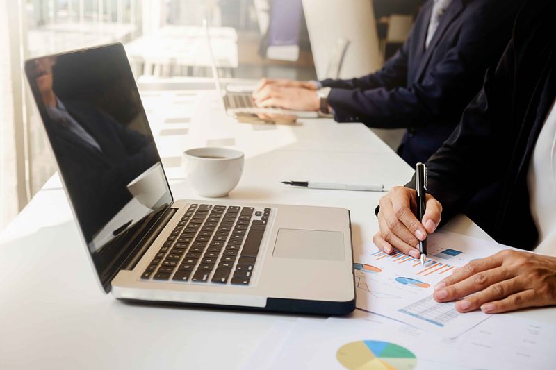 A meeting around a table with printed reports and a laptop